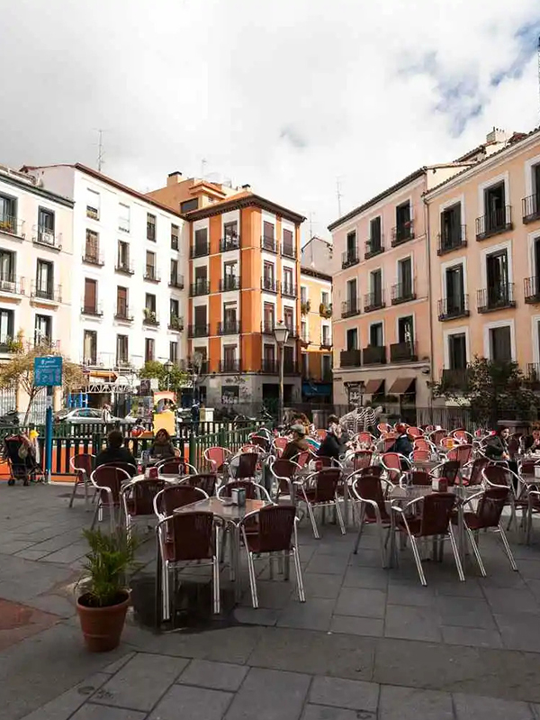 An outdoor dining area in a plaza, showcasing a restaurant with tables and chairs for patrons to relax and dine in Malasaña, Madrid